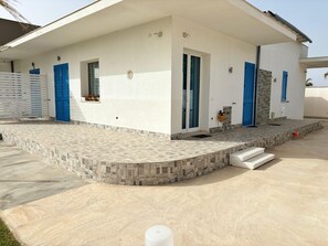 Een modern huis met een overdekt terras, een entree betegeld met stenen en blauwe deuren.