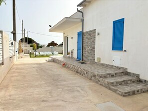 A modern building with a concrete facade, blue shutters, and a paved walkway leading to a set of steps. - Casa Vacanze - Le stanze di Eolo (Marsala)