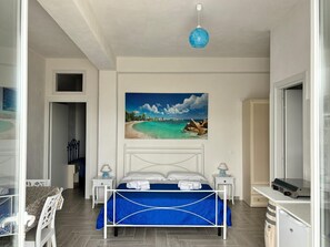 A bedroom with a bed, a painting of a beach, a ceiling light, and a wardrobe. - Casa Vacanze - Le stanze di Eolo (Marsala)