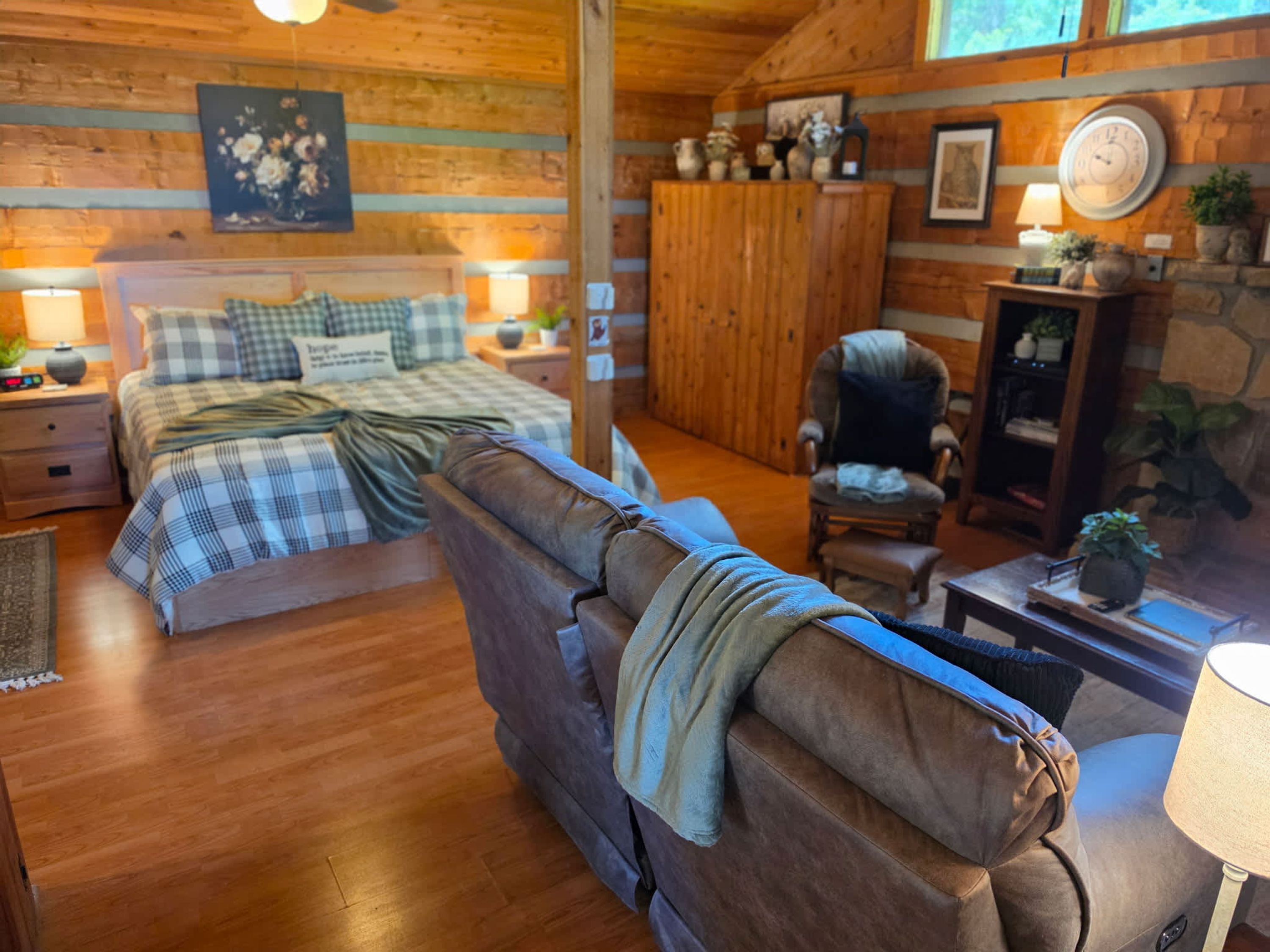 L’intérieur d’un chalet confortable, avec un lit, un canapé en cuir, une armoire en bois et une cheminée en pierre.