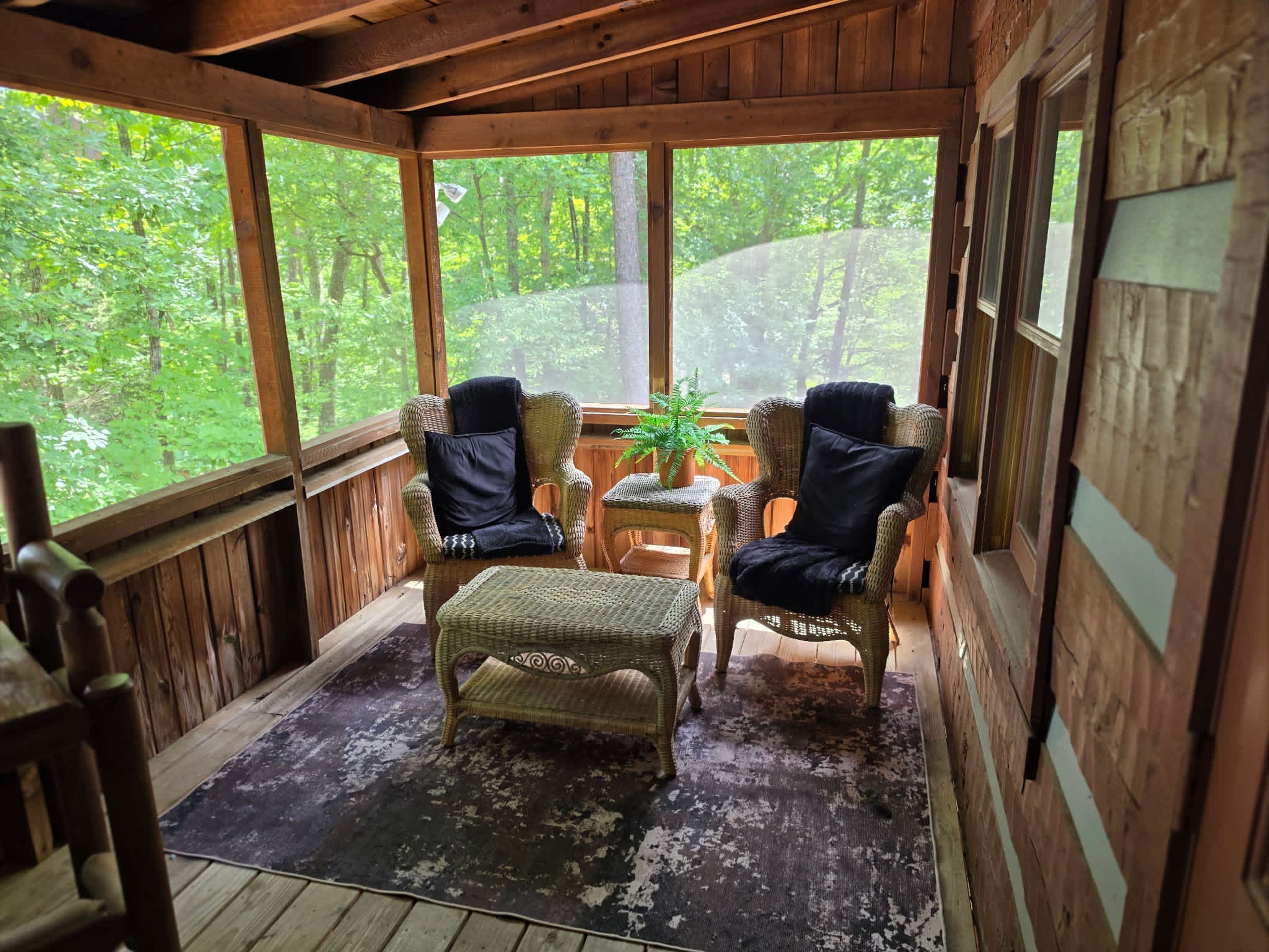 A wooden cabin with two wicker chairs, a small table, and a bench.