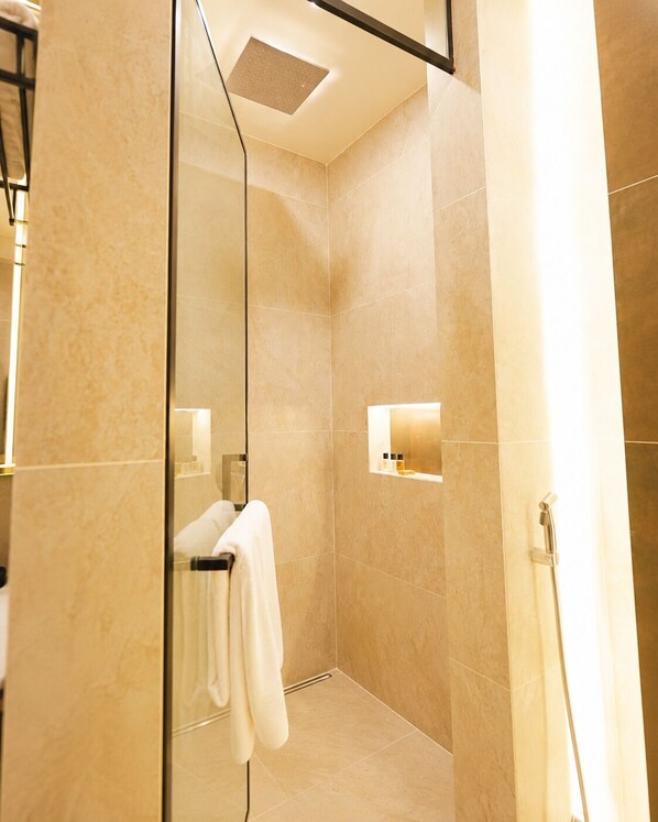 A modern bathroom with a glass shower enclosure, a towel rack, and a shelf with toiletries.