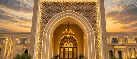 Imponente entrada con un gran arco, una lámpara central y jardines simétricos.