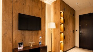 Un vestíbulo de hotel con una pared de madera, un televisor de pantalla plana, una consola de madera oscura, una lámpara de pie y una puerta oscura.