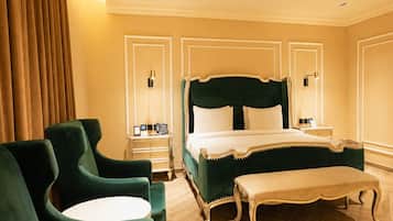 Habitación de hotel con una cama grande, dos mesitas de noche, un banco y sillones tapizados en verde.