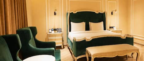 Habitación de hotel con una cama grande, dos mesitas de noche, un banco y sillones tapizados en verde.