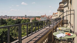 Ein Balkon mit Tisch und Stühlen, mit Blick auf eine Stadtlandschaft aus Gebäuden und Bäumen.
