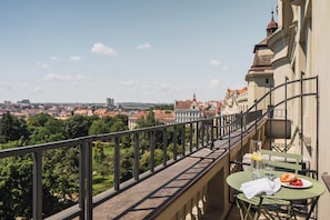 Ein Balkon mit Tisch und Stühlen, mit Blick auf eine Stadtlandschaft aus Gebäuden und Bäumen.