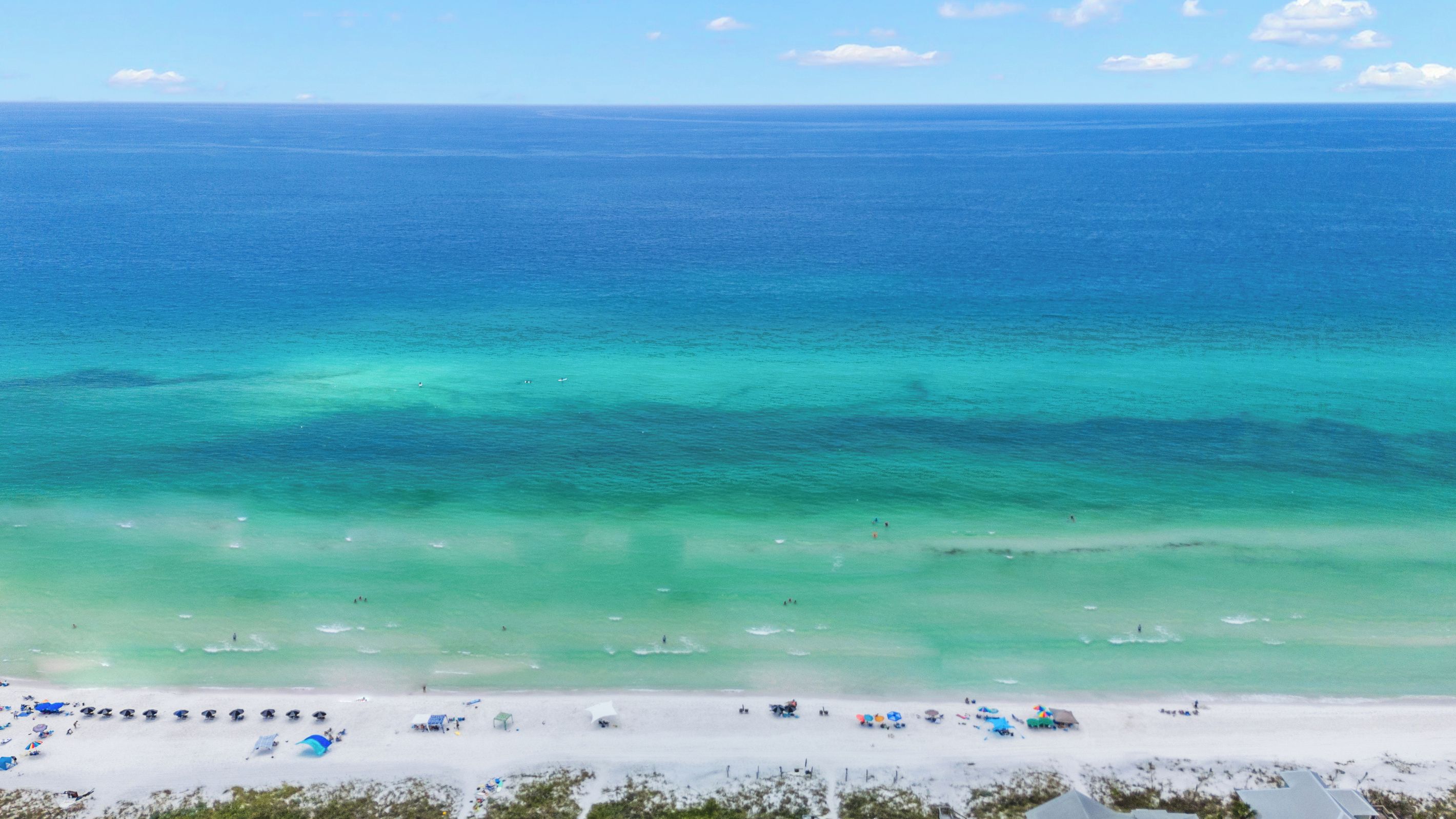 A beach with clear turquoise waters, a sandy shore, and several beach umbrellas.
