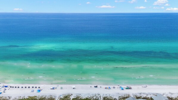 A beach with clear turquoise waters, a sandy shore, and several beach umbrellas. - Dogs OK~Community Pool~Short Walk to Beach~Grill (Santa Rosa Beach)