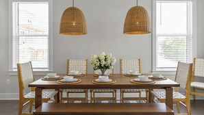 Un coin repas avec une table en bois dressée pour six personnes, entourée de chaises à assise en osier, et deux lampes suspendues en rotin.