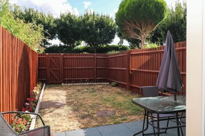 Ein Garten mit Holzzaun, Terrassentisch mit Stühlen und einem kleinen Blumenbeet.