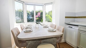 Una cuina moderna amb zona de menjador, amb un gran finestral que ofereix vistes a vegetació, un rentaplats blanc i un taulell de marbre.