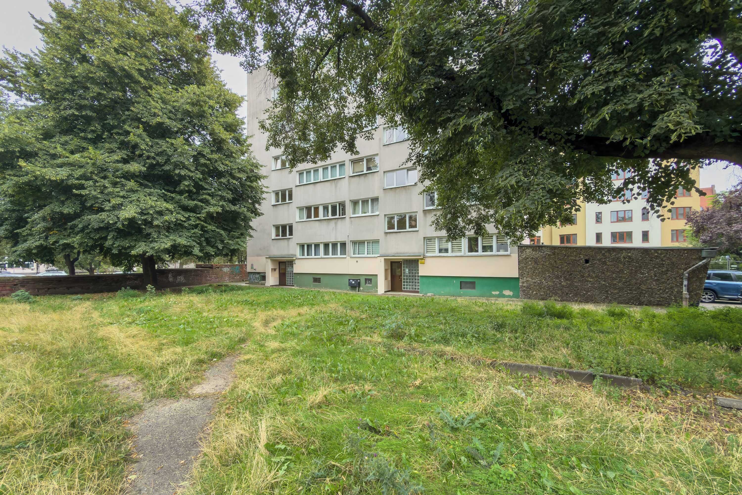 Un immeuble résidentiel à plusieurs étages, doté d’une façade verdoyante, d’un chemin pavé et d’une zone herbeuse au premier plan.