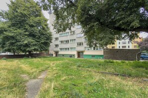 Ein mehrgeschossiges Wohngebäude mit grüner Fassade, einem gepflasterten Weg und einer Rasenfläche im Vordergrund.