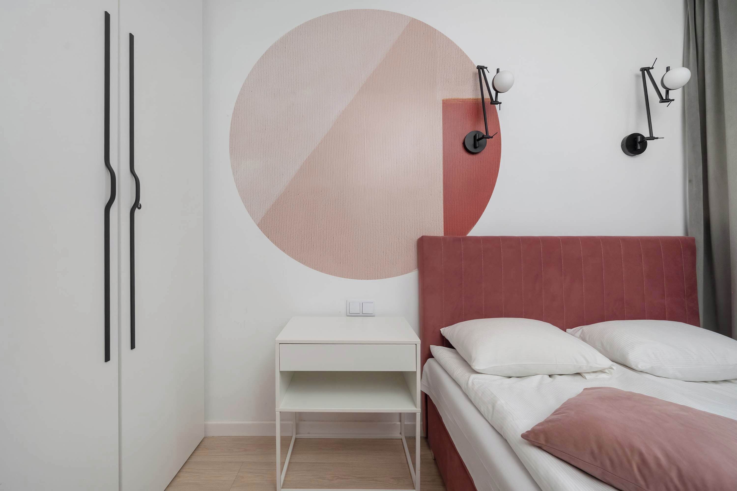 Une chambre à coucher comprenant un lit, une table de chevet, une lampe fixée au mur et une grande décoration murale abstraite.