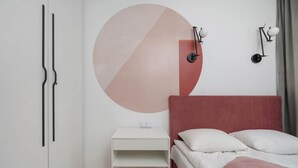 Una camera da letto con un letto, un comodino, una lampada a parete e un'ampia decorazione astratta a parete.