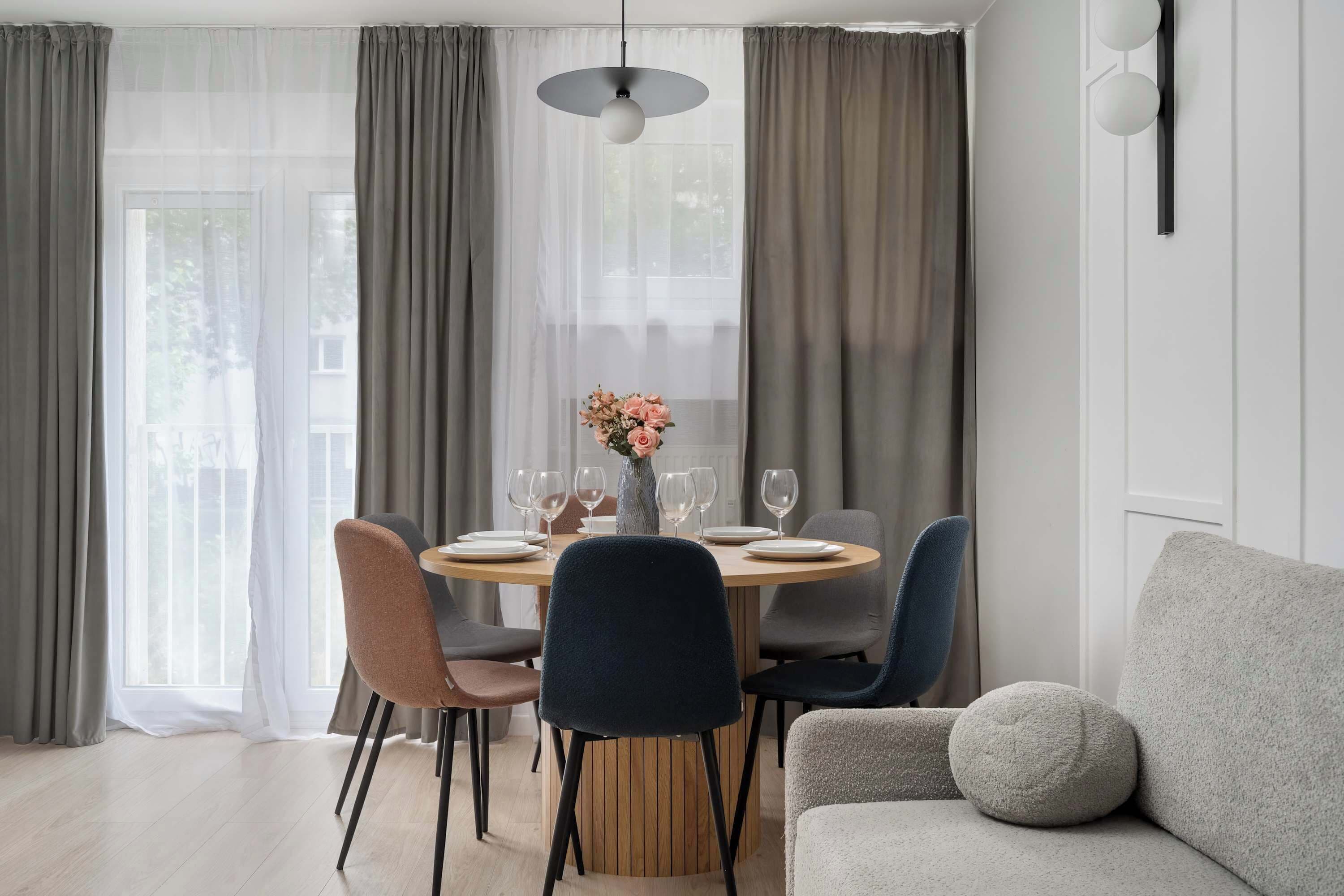Un espace repas moderne avec une table ronde, six chaises et un vase de fleurs.