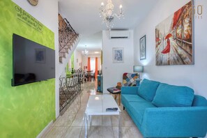 Ein modernes Wohnzimmer mit Flachbildfernseher, einem blauen Sofa, einer Deckenleuchte und einer Treppe.