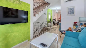Ein Wohnzimmer mit Flachbildfernseher, einer Treppe mit dekorativer Geländer und einem blauen Sofa.