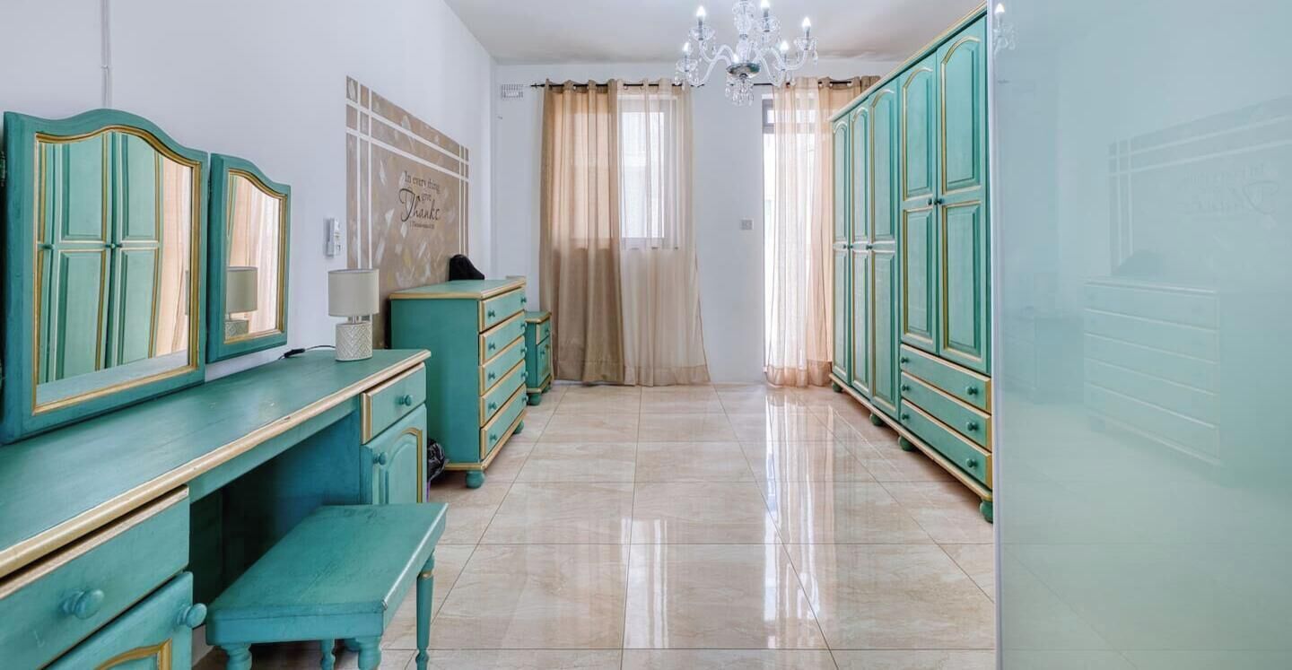 Ein Zimmer mit türkis-farbener Einrichtung, einem Kronleuchter und Blick durch einen mit Vorhängen versehenen Fensterschein.