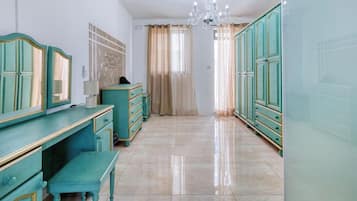 Ein Zimmer mit türkis-farbener Einrichtung, einem Kronleuchter und Blick durch einen mit Vorhängen versehenen Fensterschein.
