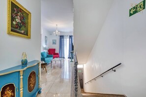 Eine Treppe mit Handlauf, ein blauer Schrank mit floralem Dekor, ein roter Sessel und eine Chandelier.