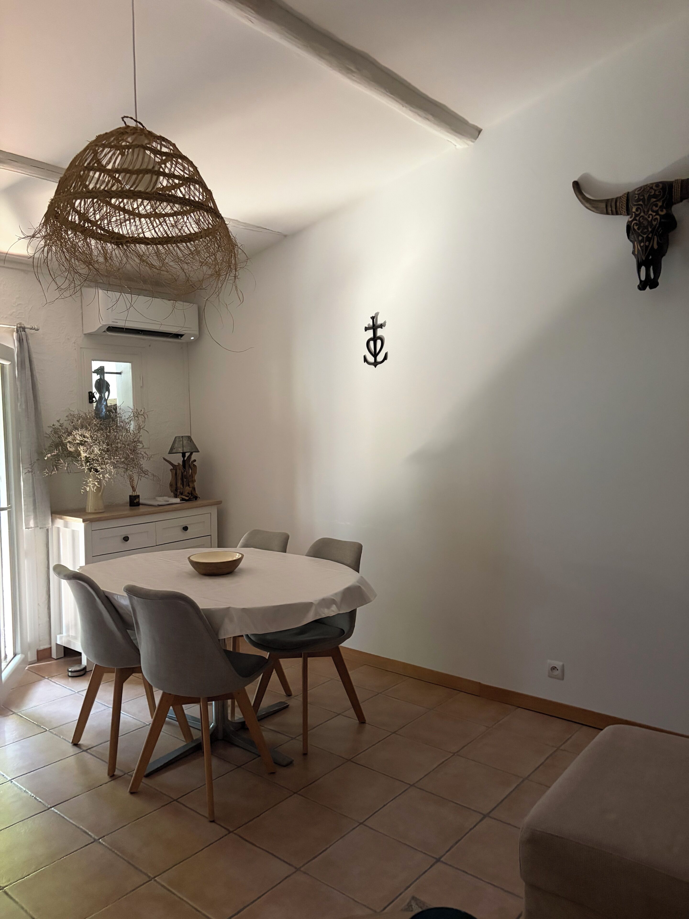 A dining area with a round table, chairs, a hanging light fixture, a wall-mounted bull's head decoration, and a wall with a symbol.