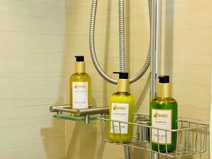 A bathroom with a shower, a glass shelf holding three bottles of Premier body wash, conditioner, and shampoo. - Chic 2-bed Family Suite Shore Residences  Pasay City MOA near airport/NAIA/Okada (Pasay City)