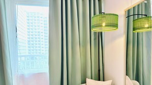Una habitación con un espejo grande, una lámpara de pie verde y vistas de un edificio a través de una ventana con cortinas.