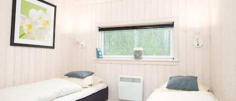A room with two beds, a window with a view of trees, a radiator, and a framed picture on the wall.