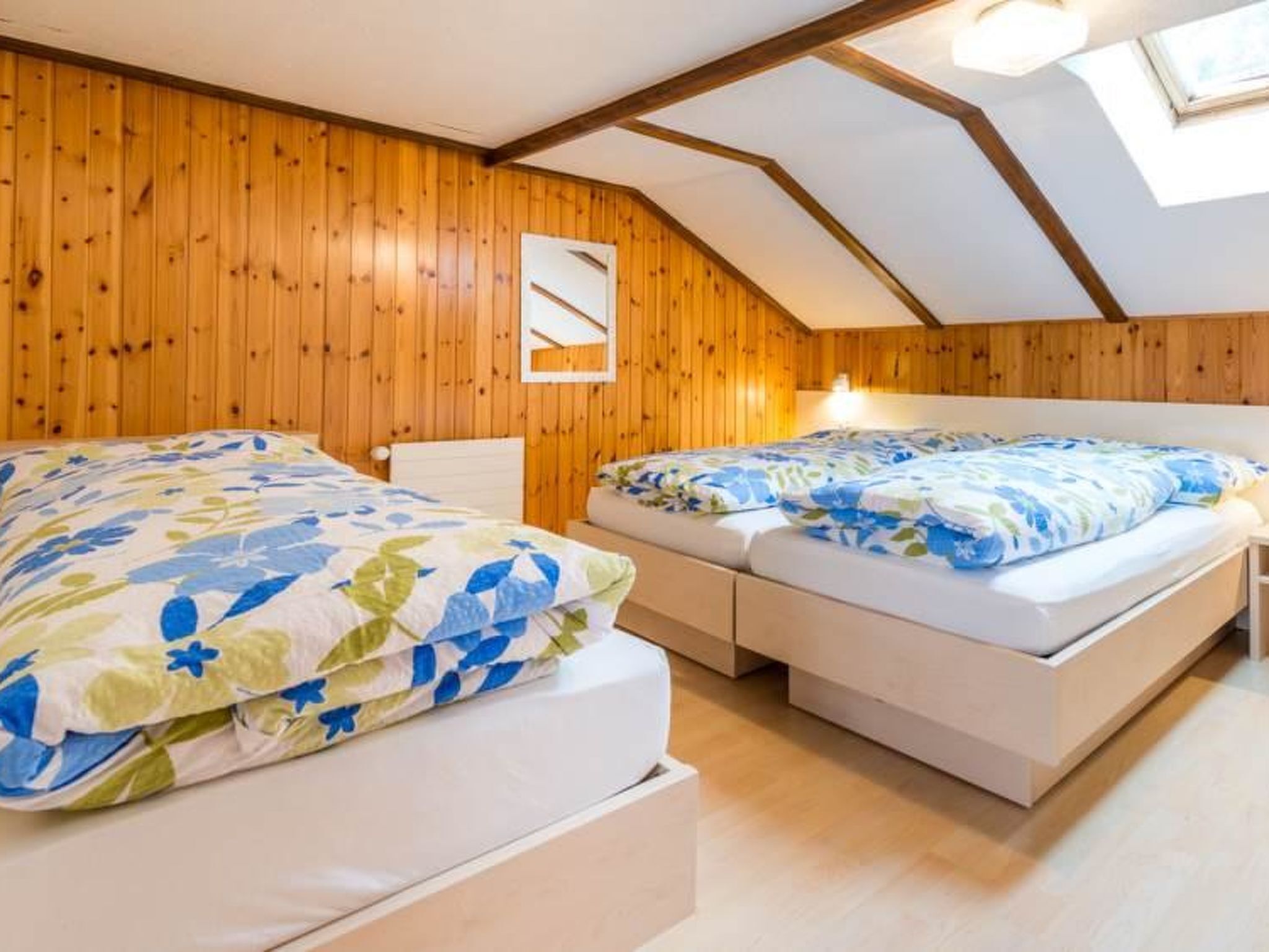 Et soveværelse med to senge, trævægge og et skråt loft.