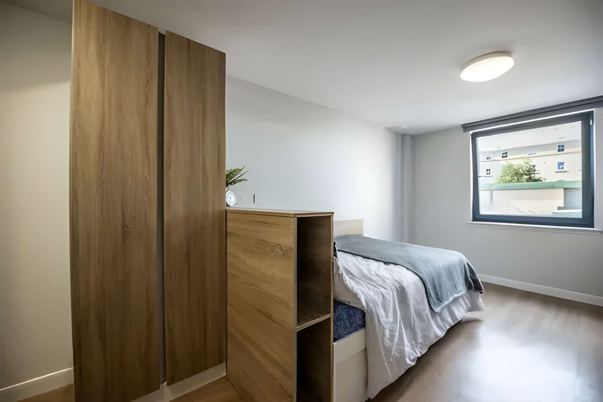 A bedroom with a bed, a wardrobe, a window, and a plant.