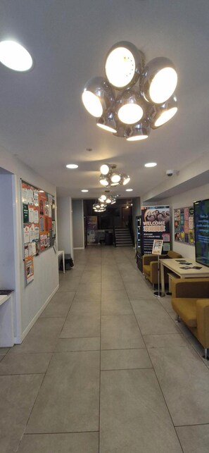 Ein Flur mit einer Rezeption, Informationsplakaten und einer Treppe zu einer anderen Etage.