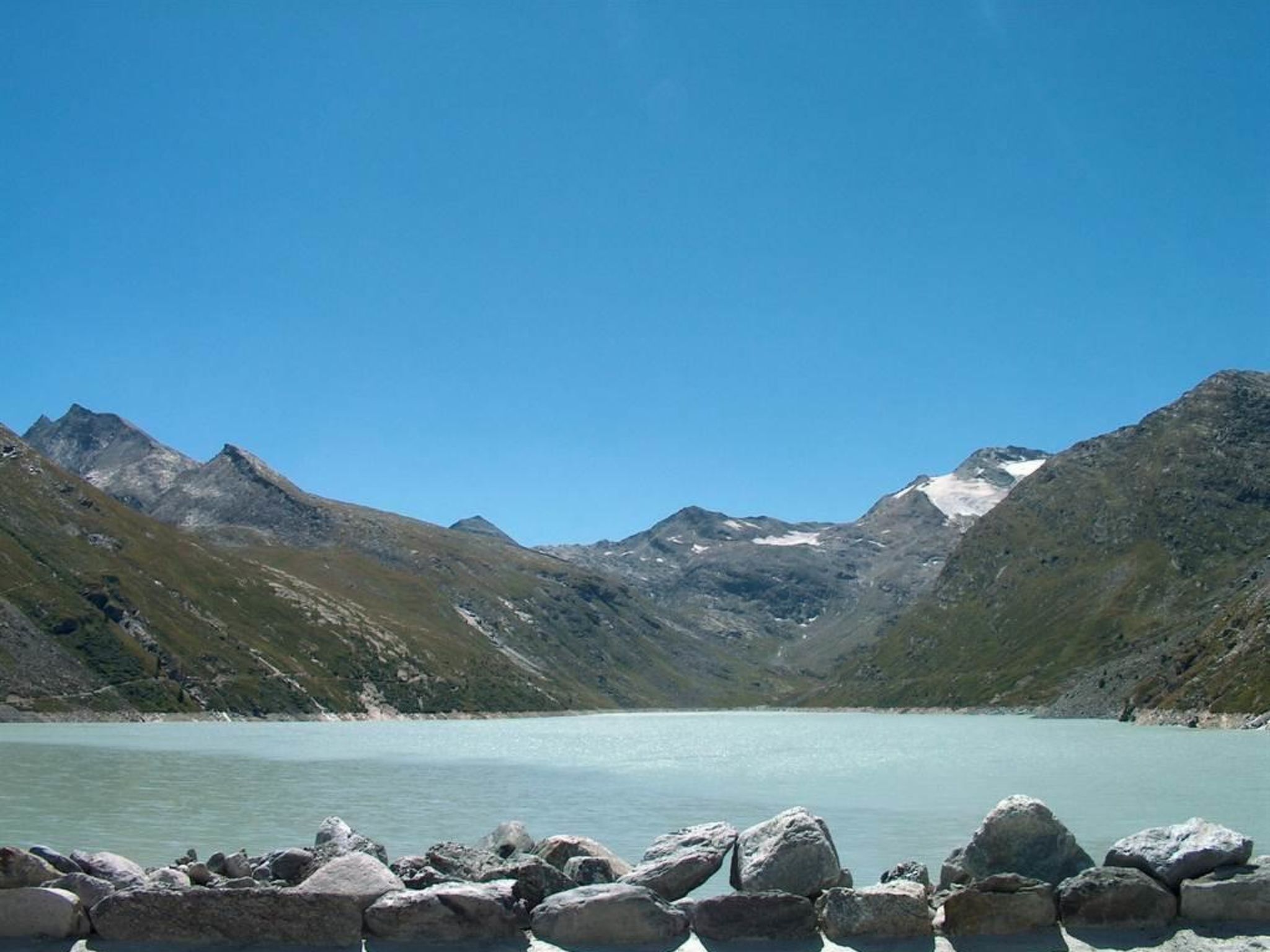 A mountainous landscape with a clear lake, rocky shoreline, and snow-capped peaks.