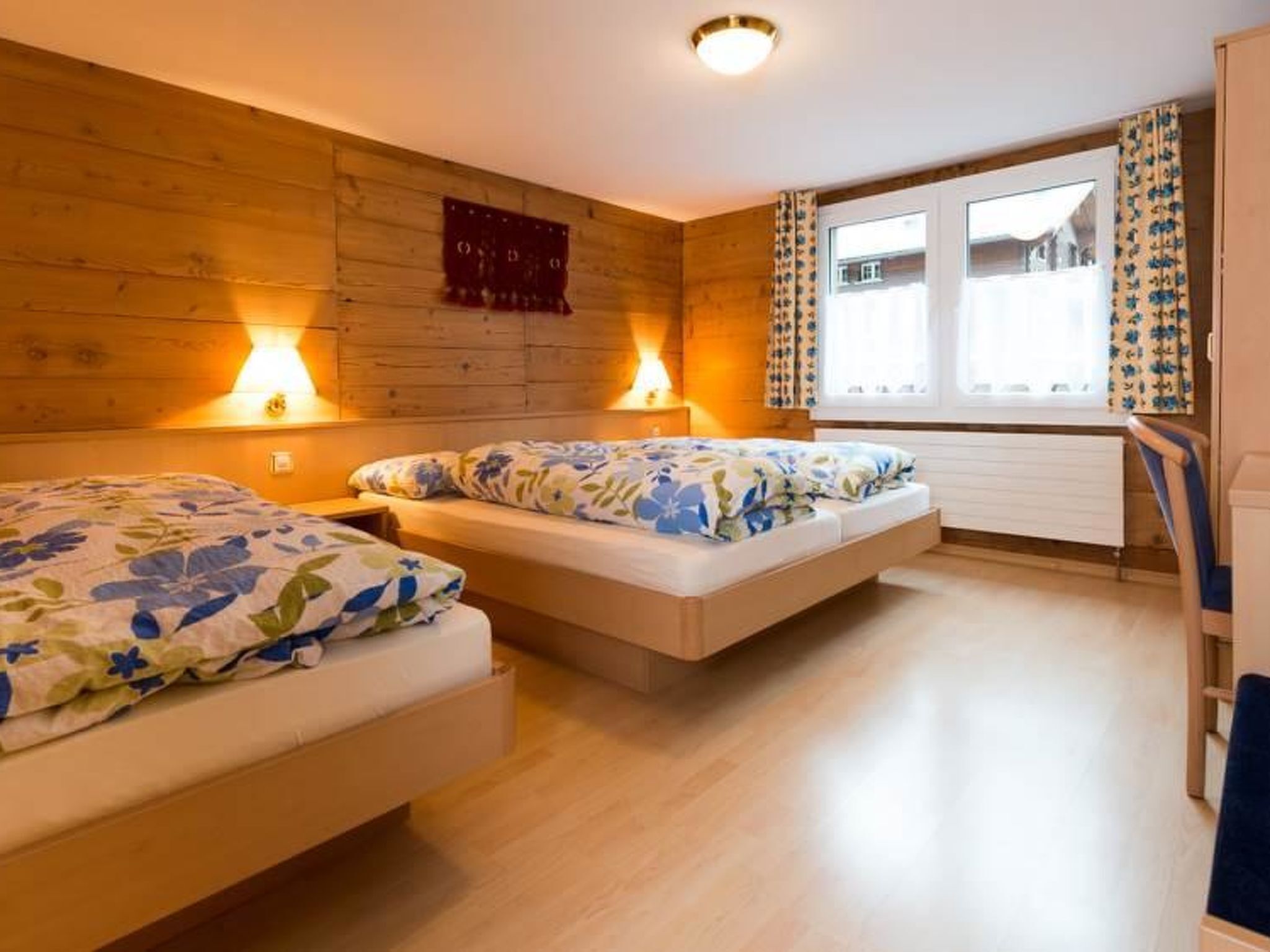 Une chambre avec deux lits, des murs en bois, une fenêtre avec des rideaux et un luminaire au plafond.