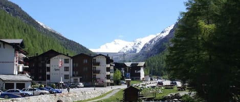 Blick auf einen Fluss mit Gebäuden, eine Person sitzt am Wasser und im Hintergrund Berge.