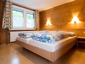 Un dormitorio con cabecera de madera, cama con ropa de cama floral, dos lámparas fijadas a la pared y una ventana con cortinas.