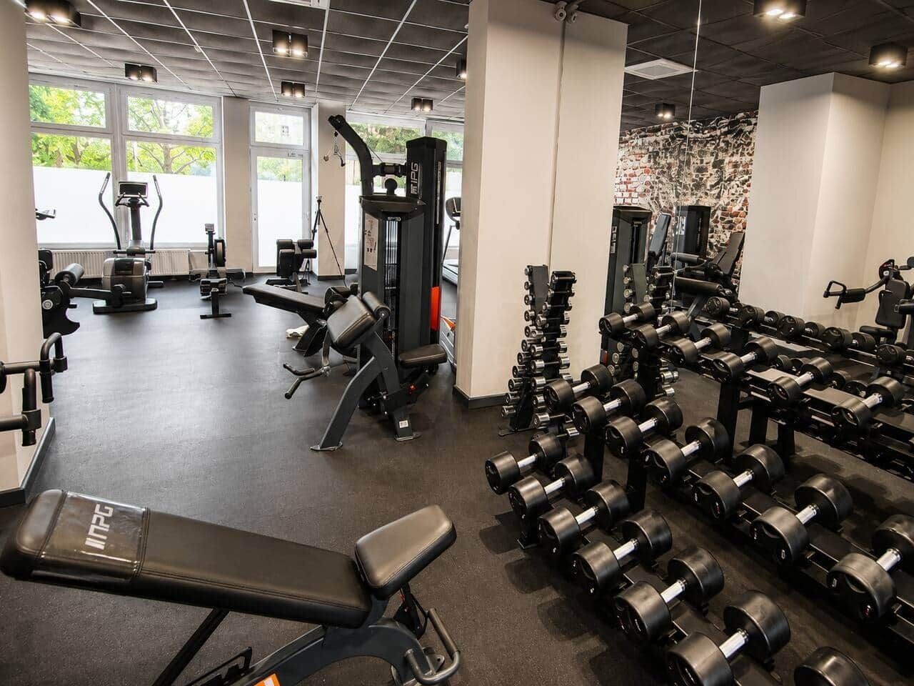Ein Fitnessstudio mit unterschiedlichen Trainingsgeräten, darunter Laufbänder, Kraftgeräte und eine Bank.