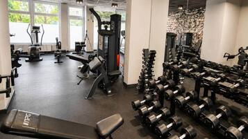 Ein Fitnessstudio mit unterschiedlichen Trainingsgeräten, darunter Laufbänder, Kraftgeräte und eine Bank.