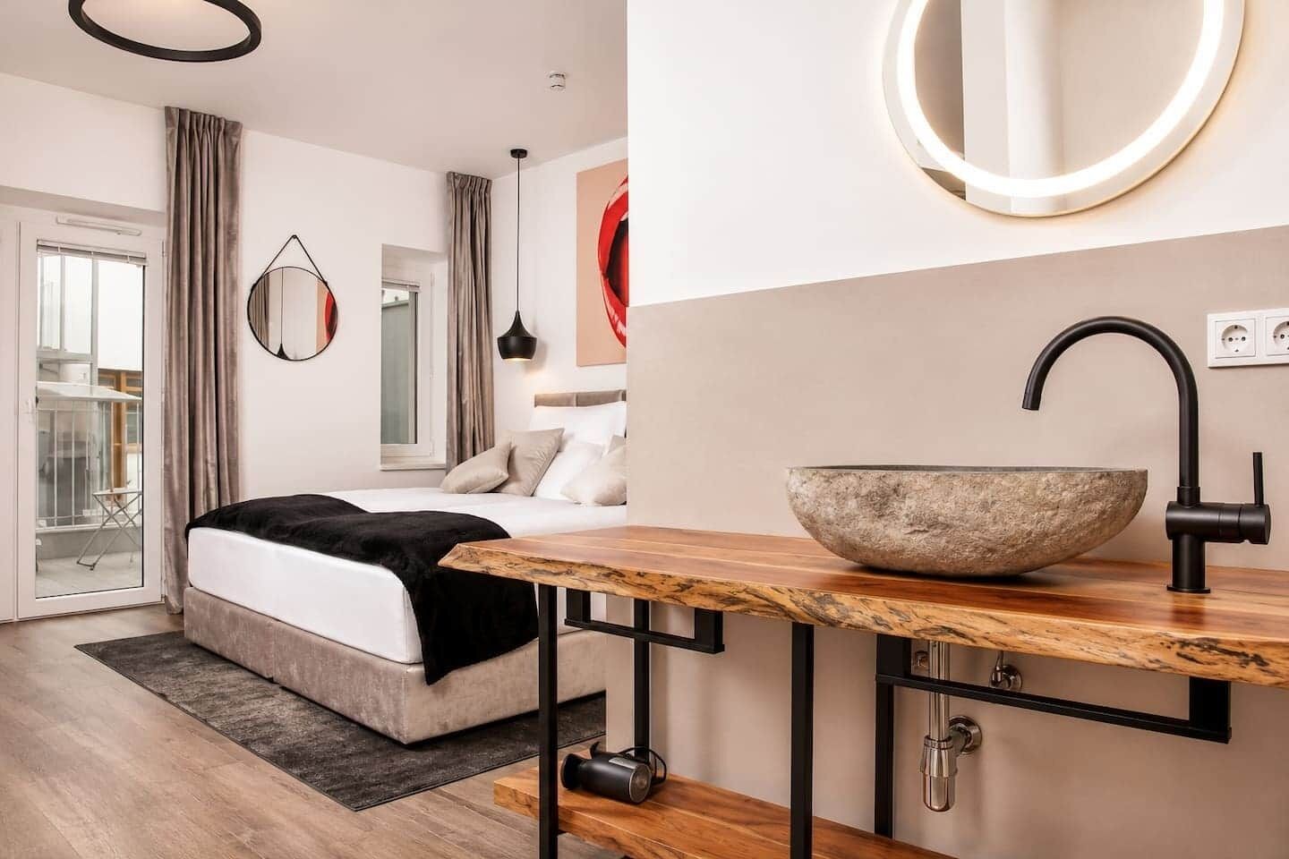 Ein modernes Schlafzimmer mit einem großen Bett, einem Nachttisch aus Holz, einem Waschbecken aus Stein und einem runden Spiegel.