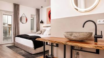 Ein modernes Schlafzimmer mit einem großen Bett, einem Nachttisch aus Holz, einem Waschbecken aus Stein und einem runden Spiegel.