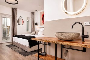 Quarto moderno com uma cama grande, mesa de cabeceira de madeira, lavatório de pedra e espelho circular.