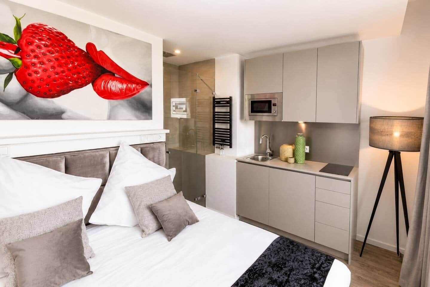 Ein modernes Hotelzimmer mit Bett, einem großen Gemälde, einer Küchenzeile und einer Stehlampe.