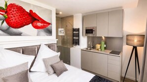 A modern hotel room with a bed, a large painting, a kitchenette, and a floor lamp. - The Faces | Compact Studio | 305 (Berlin)
