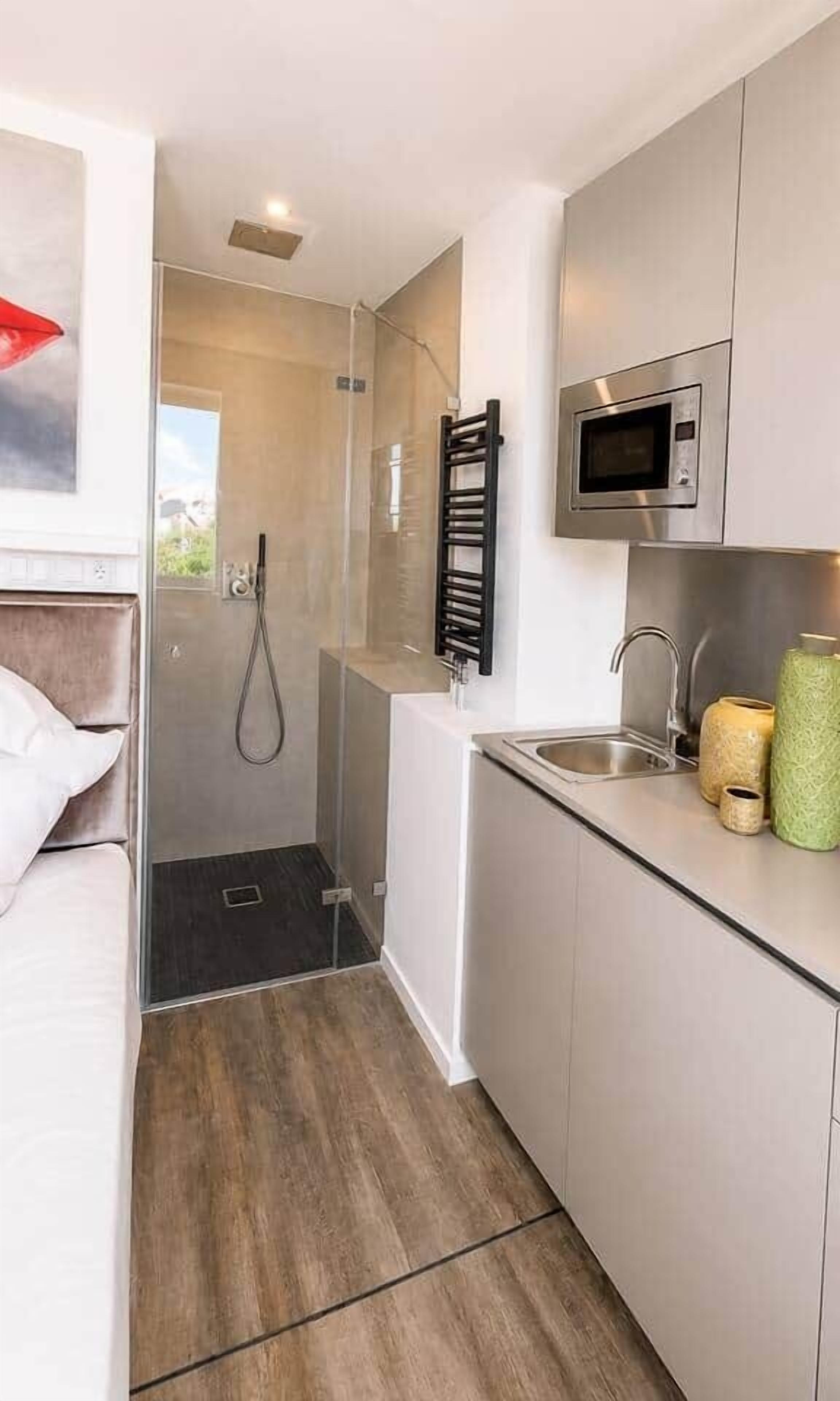 Ein kleines Hotelzimmer mit Dusche, einem Bett, einer Küchenzeile mit Mikrowelle und einem kleinen Fenster.