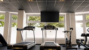 A gym with treadmills, a stationary bike, and a TV screen. - The Faces | Compact Studio | 305 (Berlin)
