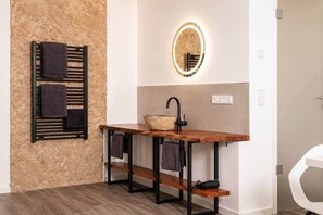 A bathroom with a wooden vanity, a round mirror with a light, a towel rack, and a white toilet. - The Faces | Compact Studio | Balcony | 002 (Berlin)