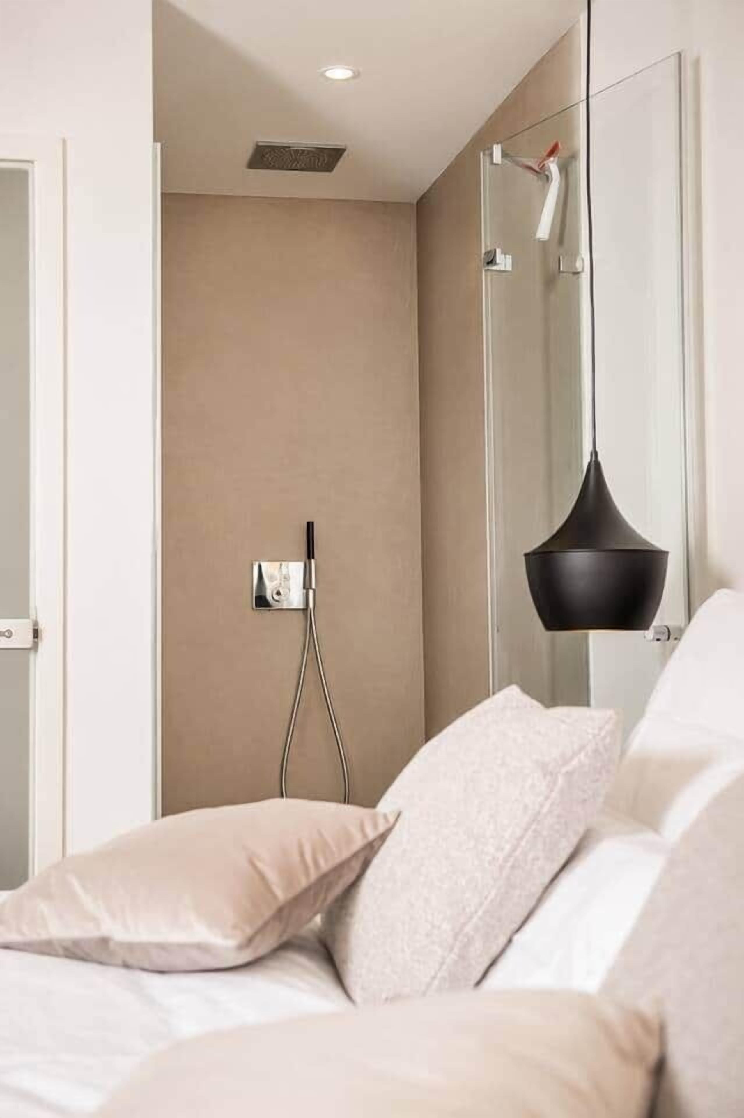 Ein modernes Schlafzimmer mit Bett, Nachttisch, Wandleuchte und einer Duschkabine.