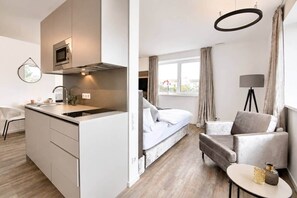 Ein modernes Hotelzimmer mit Küchenzeile, einem Bett, einer Sitzecke und Blick ins Freie.